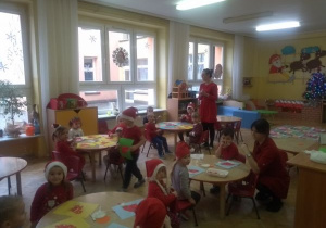 dzieci z gr VIII wyklejają kolorowym papierem czapki Mikołaja